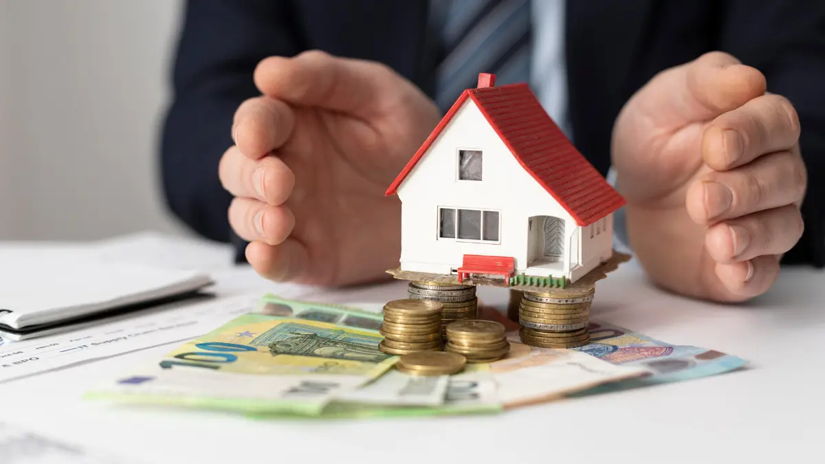 Home Affordability Calculator showing a miniature house model over coins and currency illustrating home budget and affordability estimation.