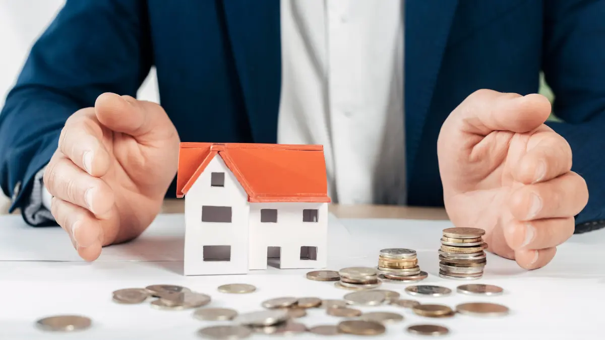 Mortgage Calculator showing hands protecting a house model with coins representing home loan savings and affordability.