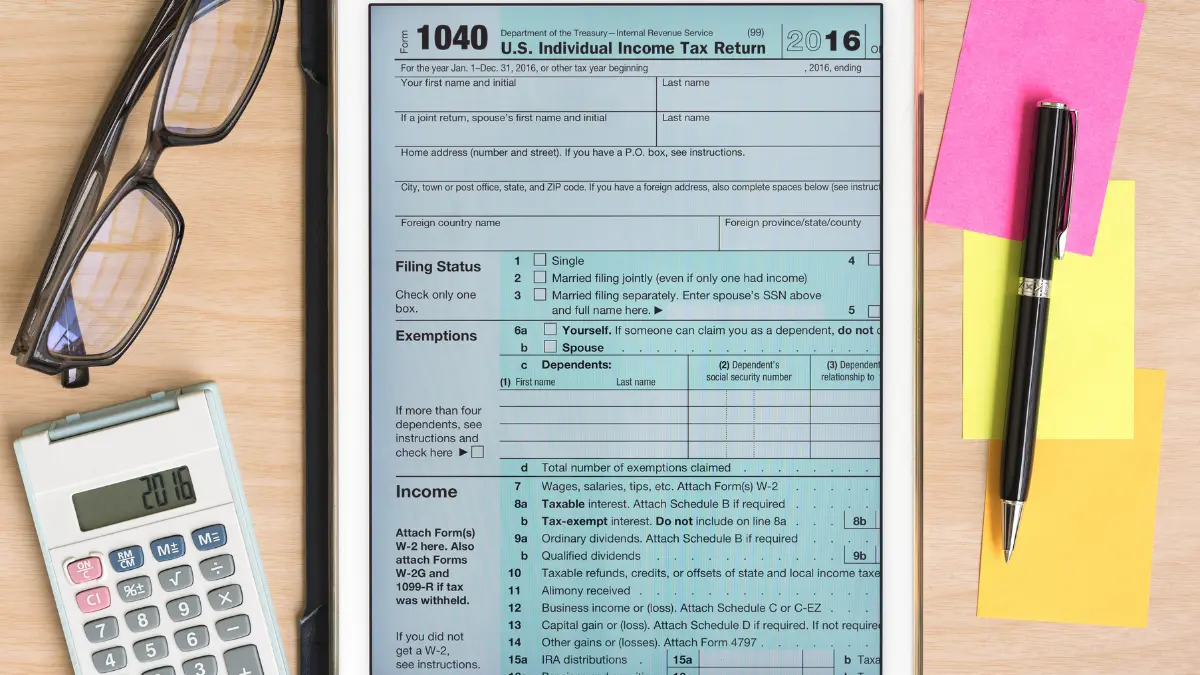 1040 Tax Form displayed on a tablet with calculator, pen, and office supplies on a desk