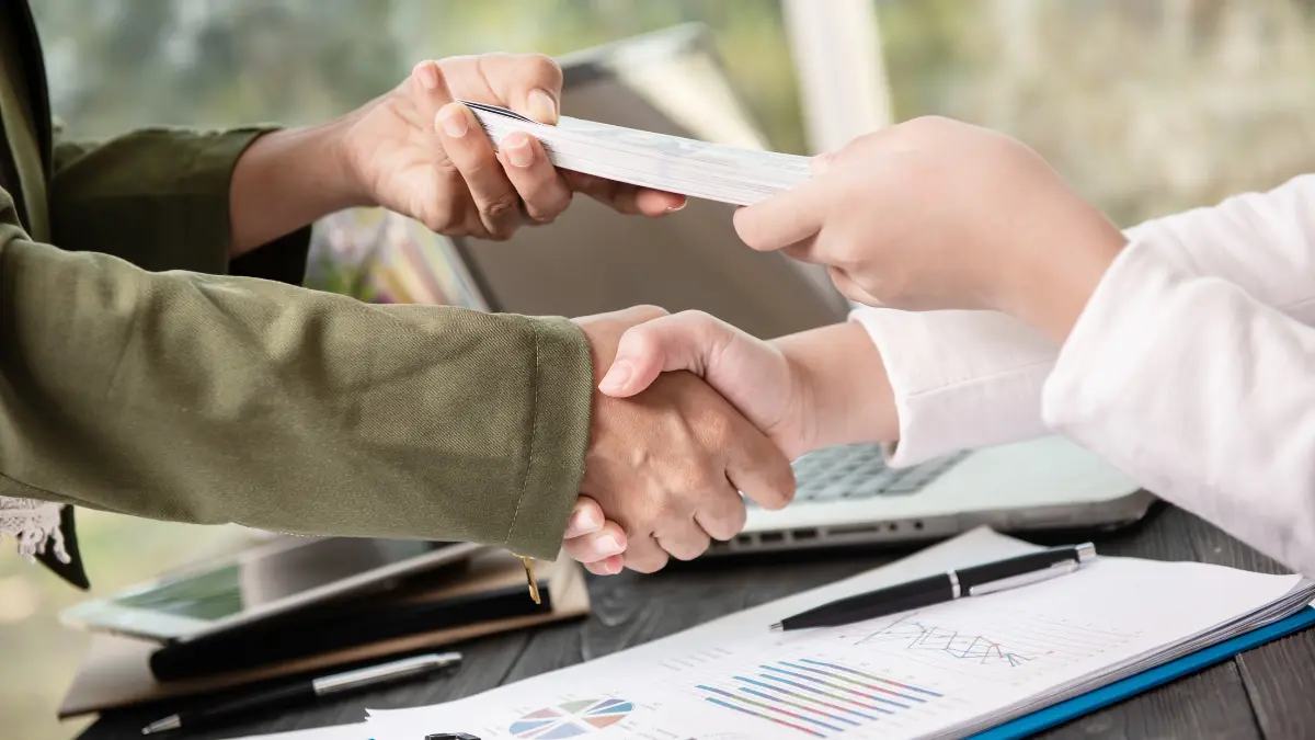 Business handshake after closing a Bond investment agreement with financial documents on desk