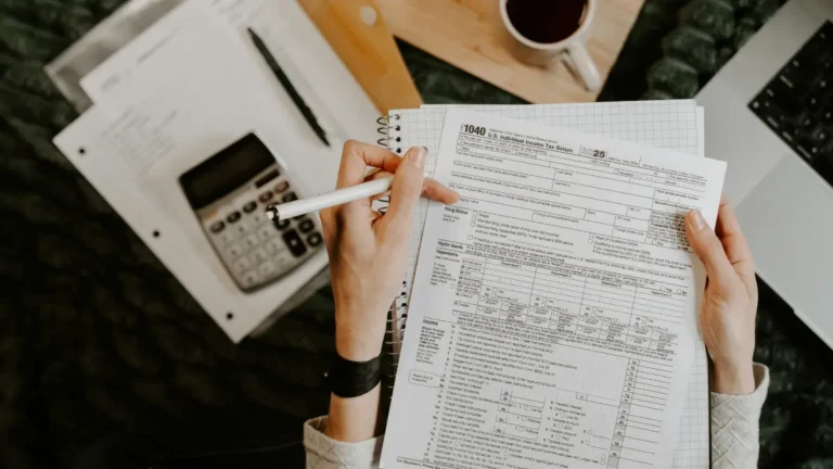 Income Tax Calculator person calculating taxes with 1040 form calculator and documents on desk